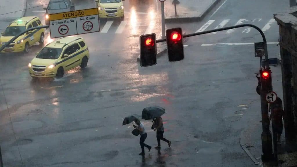 Pessoas atravessando avenida com guarda chuva durante temporal no Rio de Janeiro