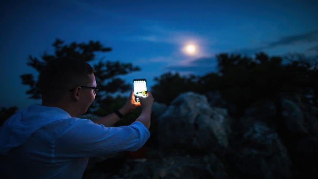 Pessoa tirando foto da lua com celular no escuro