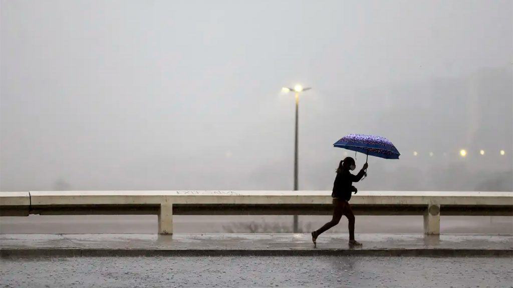 Mulher andando na chuva com guarda chuva aberto