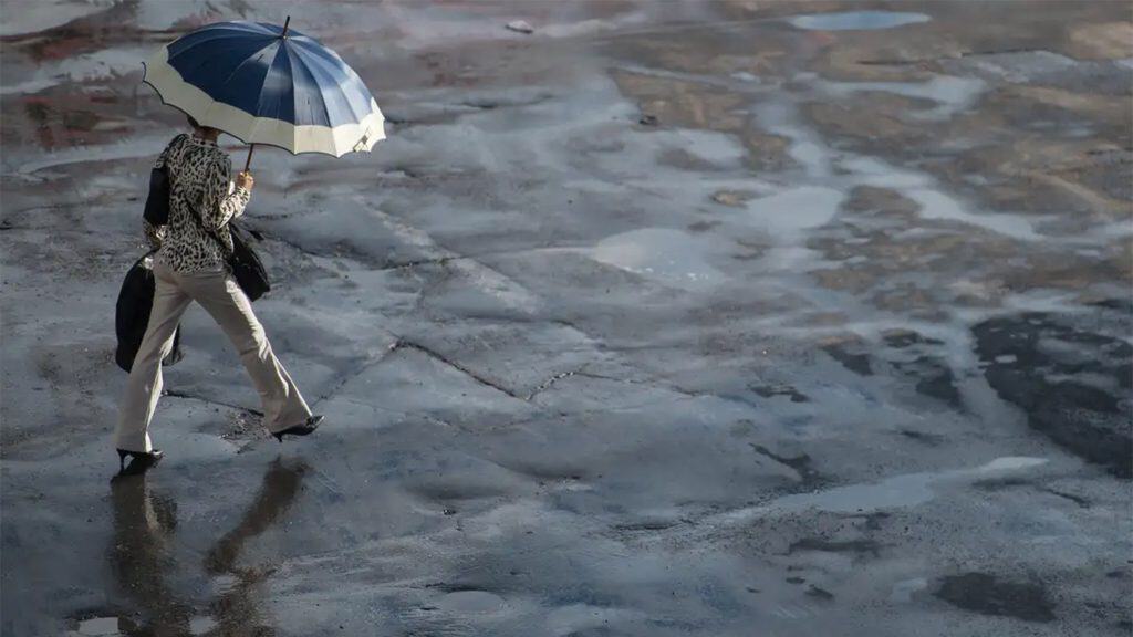 Mulher andando na com guarda chuva aberto em dia com chuva e sol